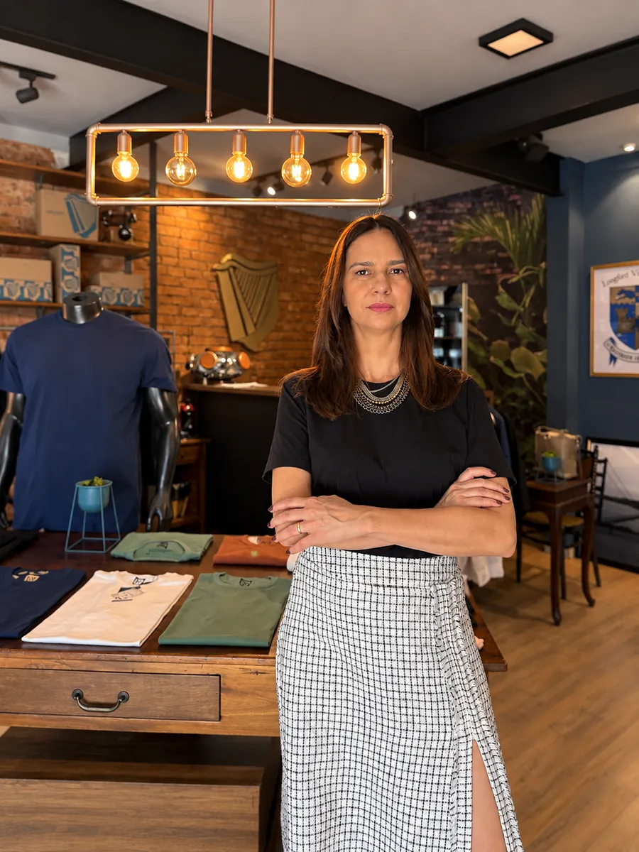 Greyci Pucci de braços cruzados na Longford, a loja dela, com as camisetas dobradas sobre a mesa atrás